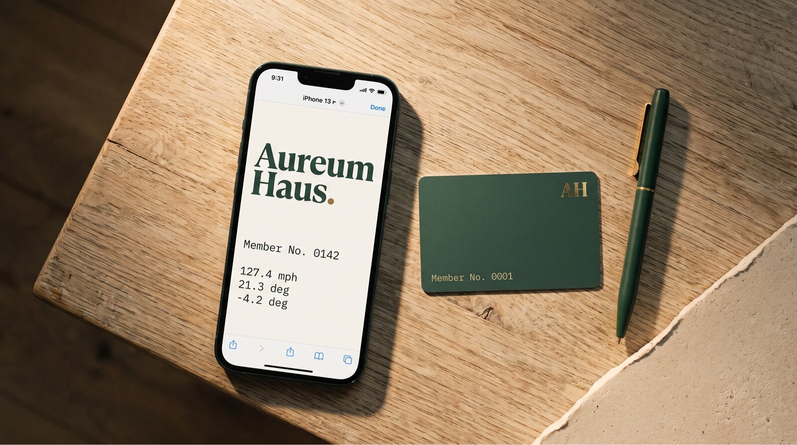 iPhone showing the Aureum Haus wordmark and a member receipt. Hemlock green member card, No. 0001, brass foil, on cedar.